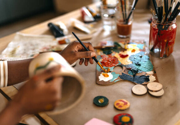Close-up woman with dreadlocks painting flower pot with watercolor paints on table at home