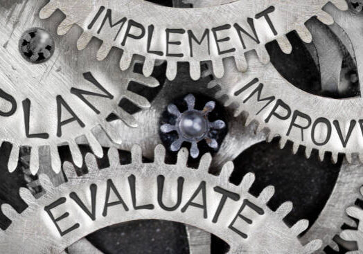 Macro photo of tooth wheel mechanism with IMPLEMENT, PLAN, IMPROVE and EVALUATE words imprinted on metal surface